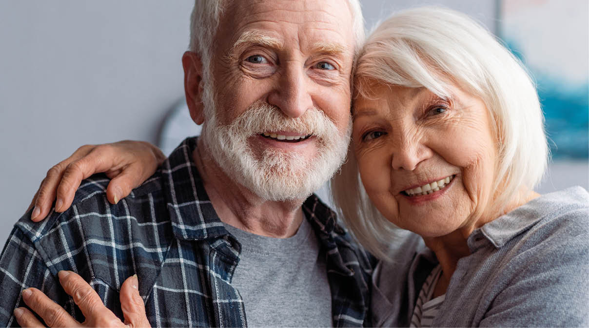 horizontal image of happy senior couple smiling and embracing while looking at camera