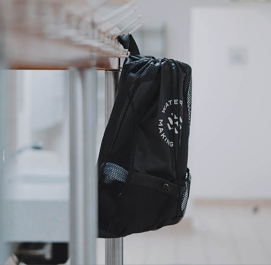 A black mesh bag with white text hangs from a metal rail in a bright, indoor space. Beschreibung von KI generiert