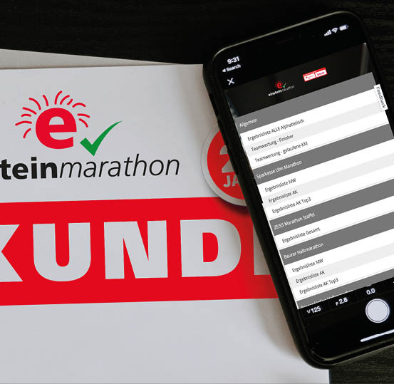 A smartphone displaying a marathon results app is placed on top of a booklet with the word “URKUNDE" and part of the text "marathon" visible. Beschreibung von KI generiert