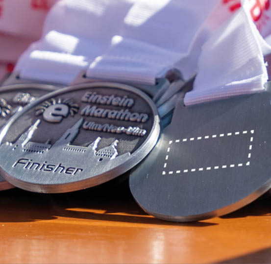 Several finisher medals with white ribbons are displayed on a wooden surface, featuring the text “Einstein Marathon Ulm/Neu-Ulm" and a cityscape design. Beschreibung von KI generiert