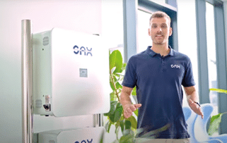 A person wearing a navy blue polo shirt stands next to a white device mounted on a metal pole in a bright room with large windows and plants. Beschreibung von KI generiert