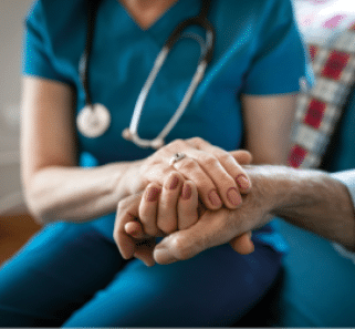 A person wearing medical scrubs and a stethoscope gently holds the hand of another person in a comforting gesture. Beschreibung von KI generiert