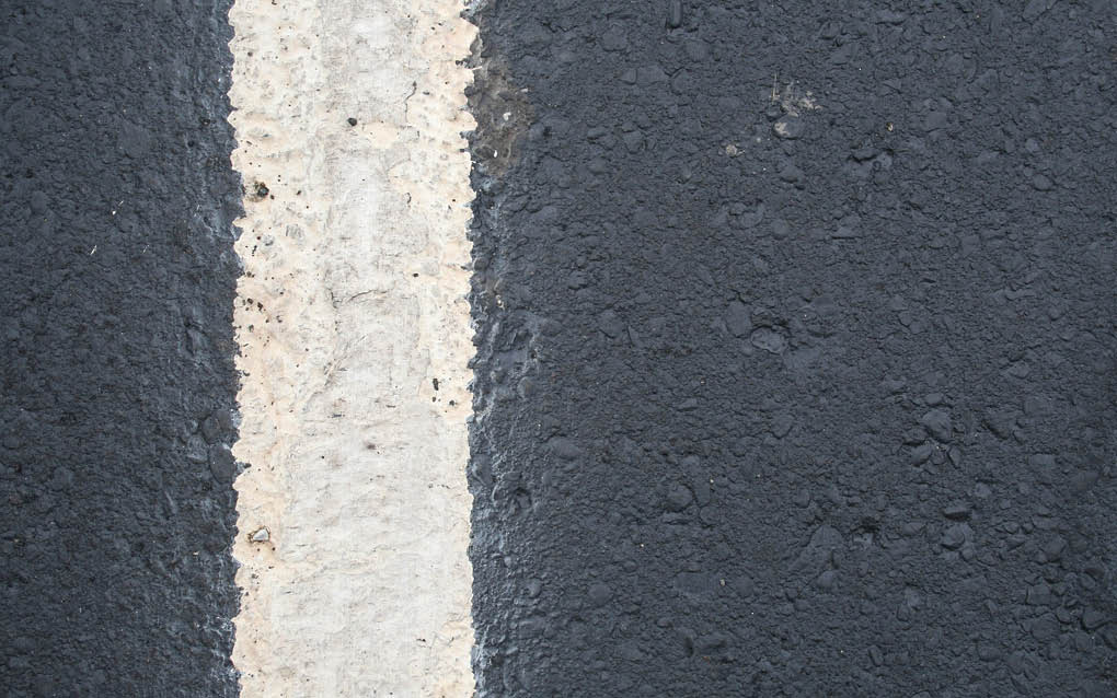A close-up view of a worn white line painted on a dark asphalt road surface. Beschreibung von KI generiert