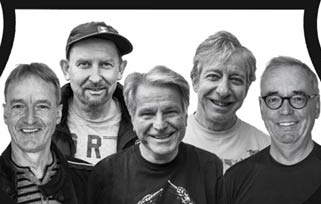 Five adults stand closely together smiling, with one wearing a cap and another wearing glasses, all dressed casually against a plain white background. Beschreibung von KI generiert