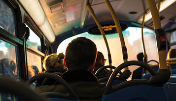 Several people are seated inside a bus, viewed from behind, with sunlight coming through the windows. Beschreibung von KI generiert
