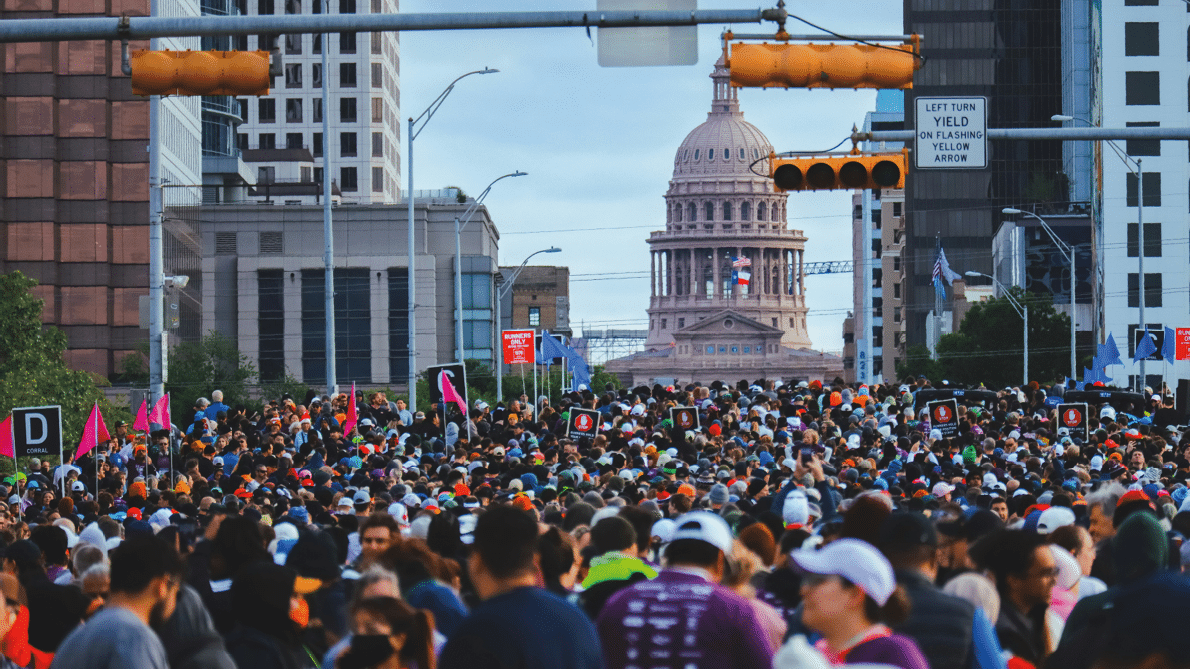 A large crowd of people gathers in a city street with a prominent domed government building visible in the background. Beschreibung von KI generiert