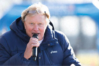 A person wearing a dark blue jacket and glasses on their head is speaking into a microphone outdoors. Beschreibung von KI generiert