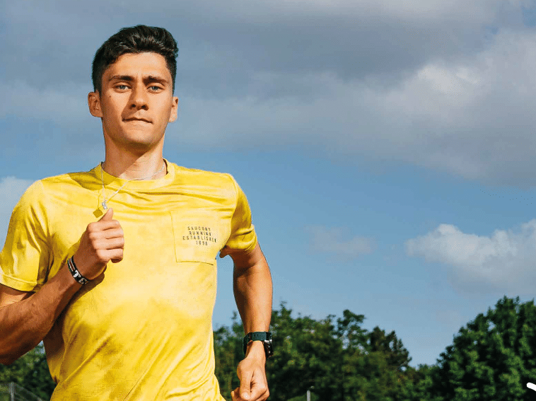 A person wearing a yellow shirt is running outdoors with a focused expression against a partly cloudy sky and trees in the background. Beschreibung von KI generiert