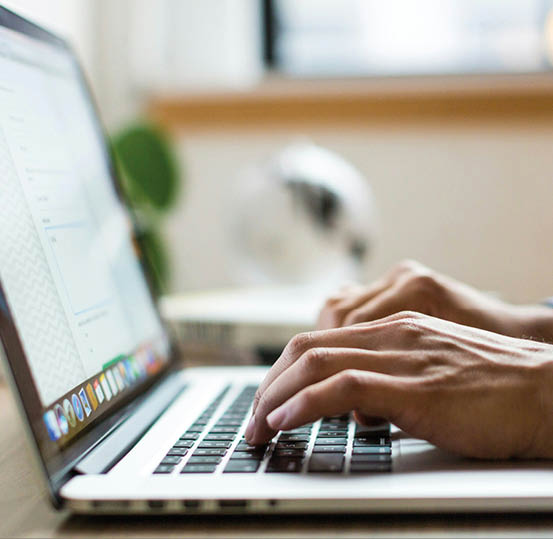 A person is typing on a laptop keyboard in a softly lit indoor setting with a blurred background. Beschreibung von KI generiert