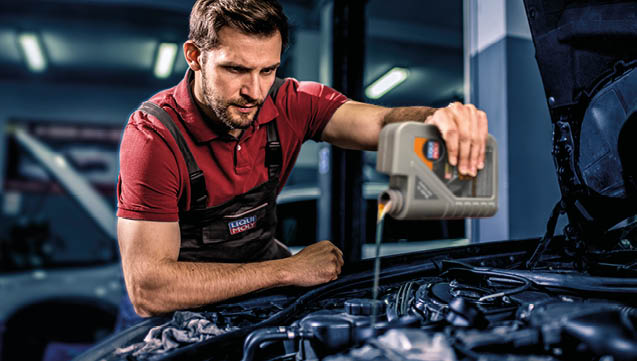Young auto mechanic changing oil on car engine at auto repair shop.